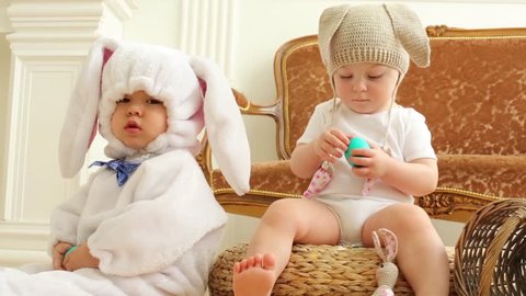 Baby boy and girl in costumes of rabbits sit. Girl cleans green egg