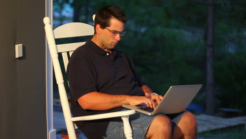 A man uses his laptop outside on the porch.