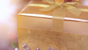 Opening a Christmas and New Year golden gift box with a blinking bauble inside, close up. Presenting a Christmas bauble. Abstract Blurred Bokeh Background. New Year decoration. HD video footage 1080p
