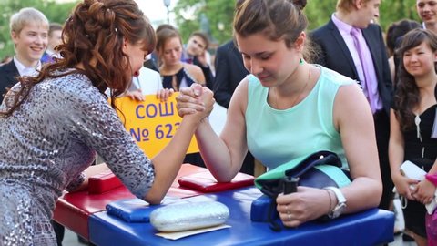 MOSCOW, RUSSIA - JUN 23, 2013: The girls graduates in dresses are arm wrestling on street at Graduate-2013.