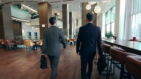 Camera following two businessmen walking along hotel lobby and discussing issues