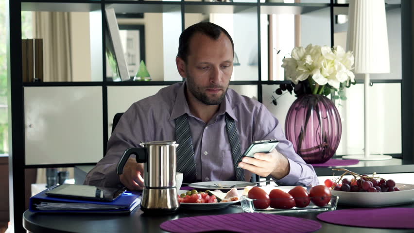 Handsome businessman with smartphone during breakfast by the table
