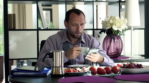 Handsome businessman with smartphone during breakfast by the table
