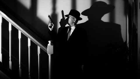 Deep shadows surround a man with a gun slowly walking up a staircase.