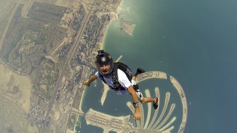 Two skydivers jump together from a helicopter before skydiving in the air over Dubai cityscape, POV