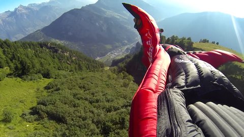 A skydiver in a wingsuit gliding in the air over a green landscape, POV