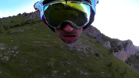 A skydiver in a wingsuit gliding in the air over a green mountain landscape, POV