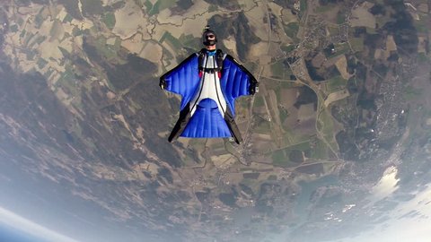 Two skydivers in wingsuits jump from a plane before gliding in the air over a landscape, POV