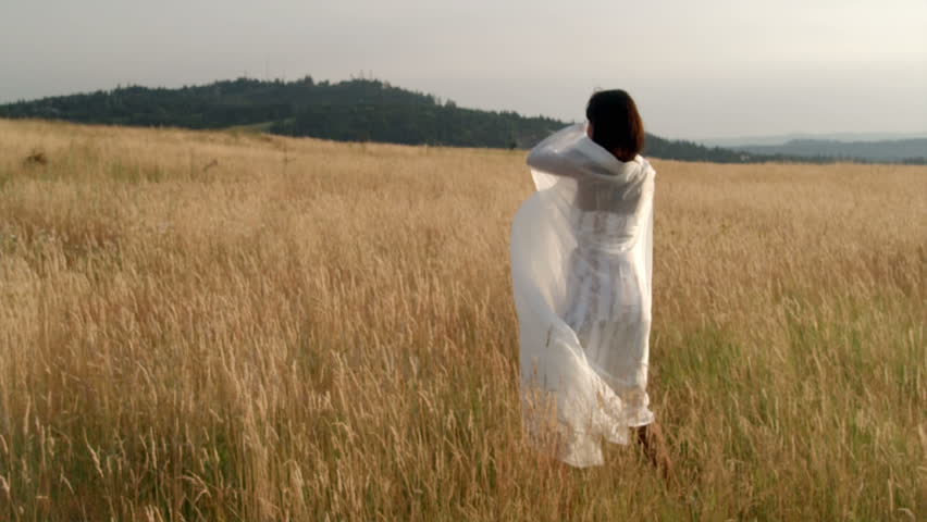 A woman waves a sheer white sheet while moving around a wheat field.