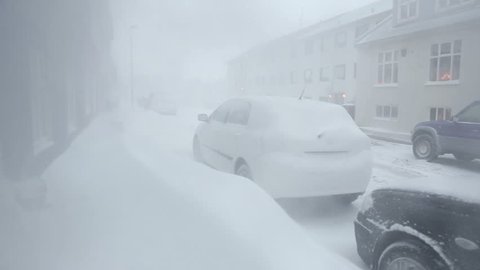 Whiteout blizzard and snowdrifts blocking sidewalk and cars in residential neighborhood during snow storm