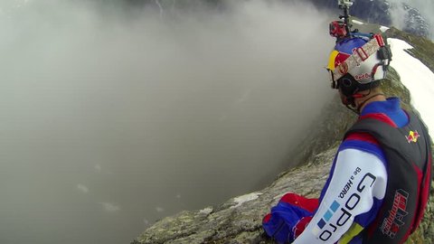A base jumper in a wingsuit jumps down from a cliff, gliding down over a green mountain landscape, POV