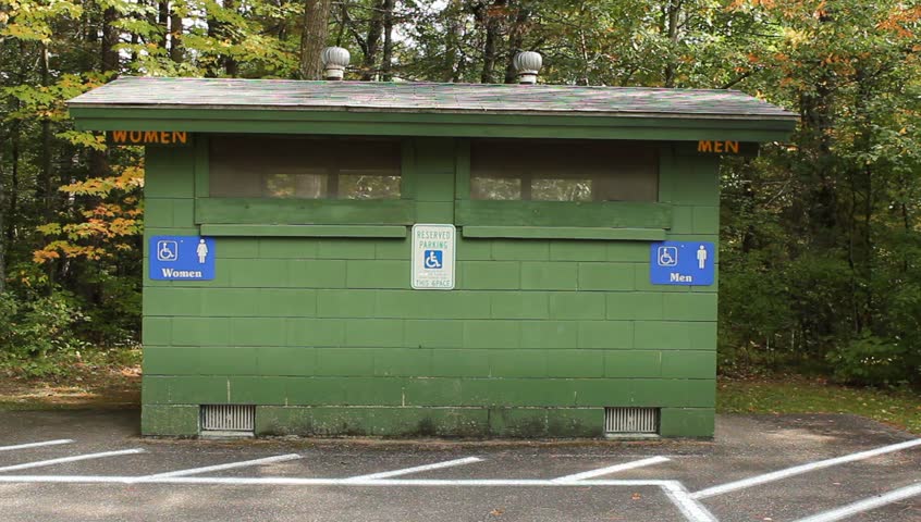 Senior man hurries to a public outhouse in the park