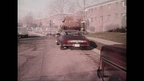 UNITED STATES LATE 1970s - A small maroon car is parked outside of apartment complex. Its driver starts the engine.
