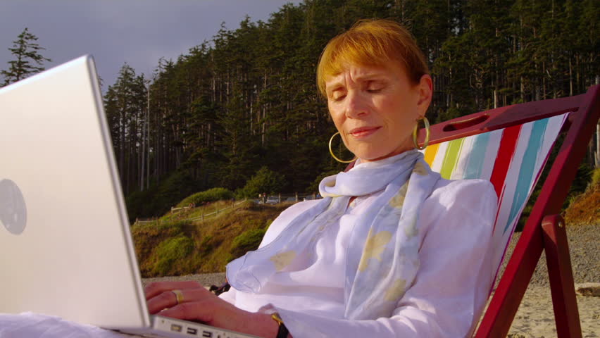 A grandmother uses her laptop on the beach. 