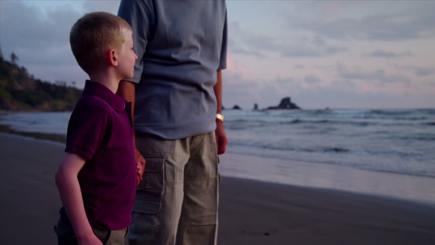A young boy and his grandfather walk on the beach at sunset.