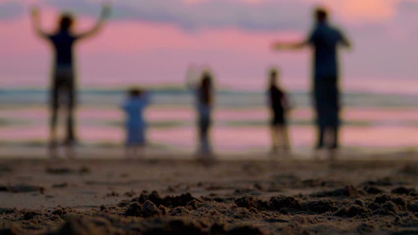 Grandparents and grandchildren do jumping jacks on the beach at sunset. 