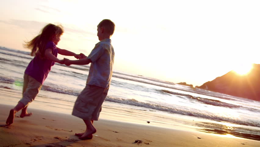 Two children dance on the beach at sunset. 