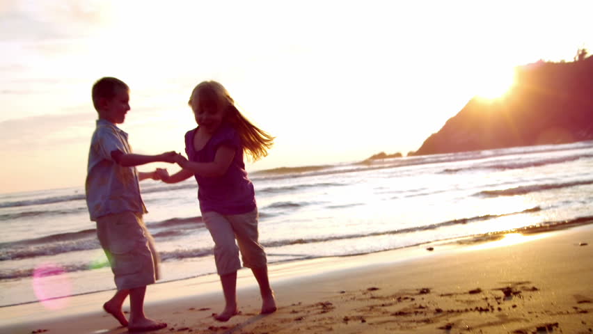 two children dance on the beach at sunset. lens flare. 