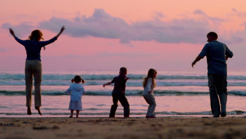 Three children and two adults jump on the beach at sunset. 