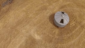 Aerial footage of vintage harvester, harvesting hay paddock in rows, around huge paddock in drought stricken dry land farming area of Australia and filling grain silo read for stock piling