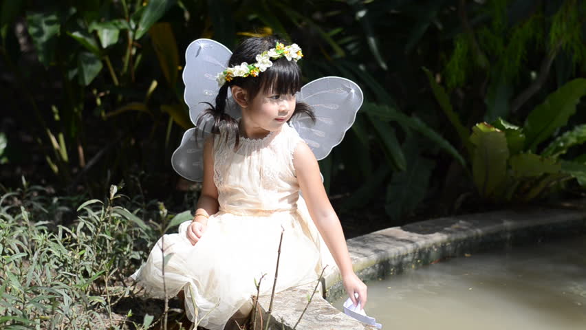 Little girl floating paper boat in the park