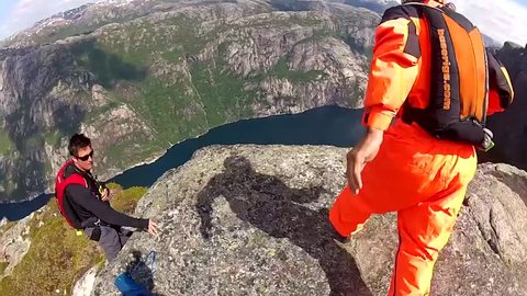 Two base jumpers leaps off from a cliff before gliding down in the air over a river, POV