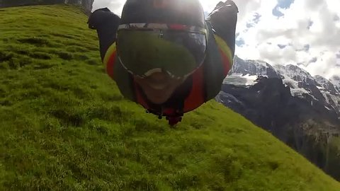 A base jumper in a wingsuit swiftly gliding in the air in a green mountain landscape, POV