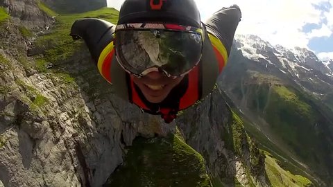 A base jumper in a wingsuit gliding down in the air in a mountain landscape, POV