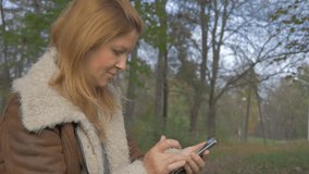 Woman using mobile phone outdoors 1080p HD video - Casual blond woman typing  on smart phone in nature 1920X1080 FullHD footage
