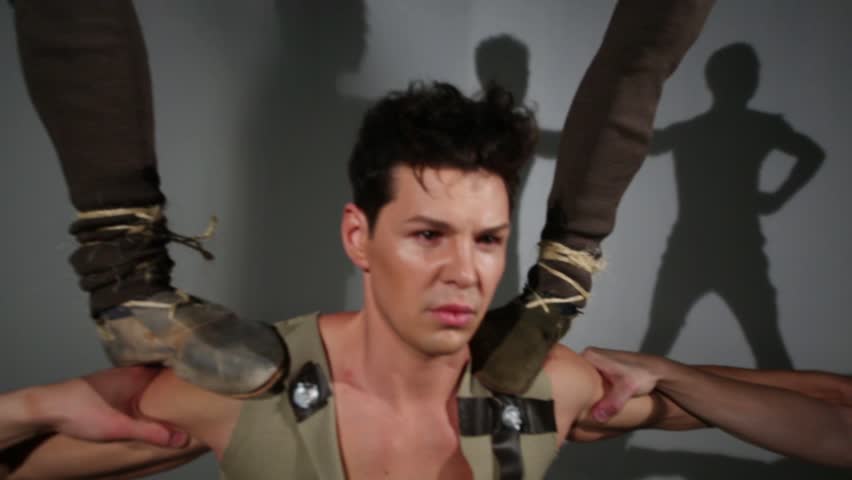 Seven guys in medieval costumes do acrobatic pyramid in studio with lamps