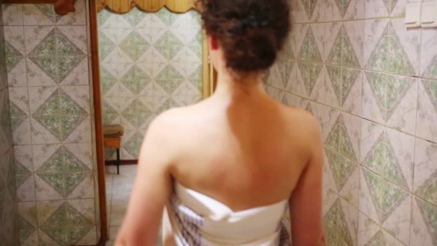 Back of young woman wrapped in sheet entering in spacious sauna