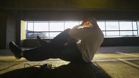 4K Slow motion clip of a hooded athlete finishing his workout with sit ups in a gritty urban environment, shot on RED EPIC