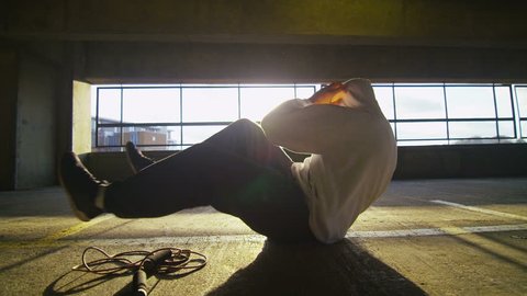 4K Slow motion clip of a hooded athlete finishing his workout with sit ups in a gritty urban environment, shot on RED EPIC