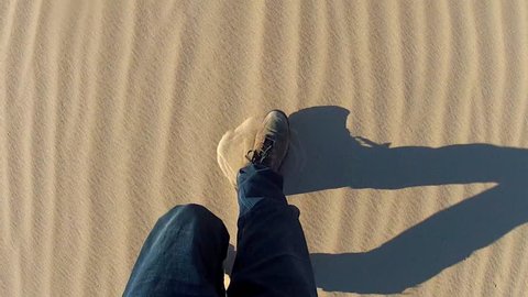 High angle shot of legs and feet of a man walking in a sandy desert. Handheld shot showing hiker and shoes kicking up sand as he shuffles and walks.