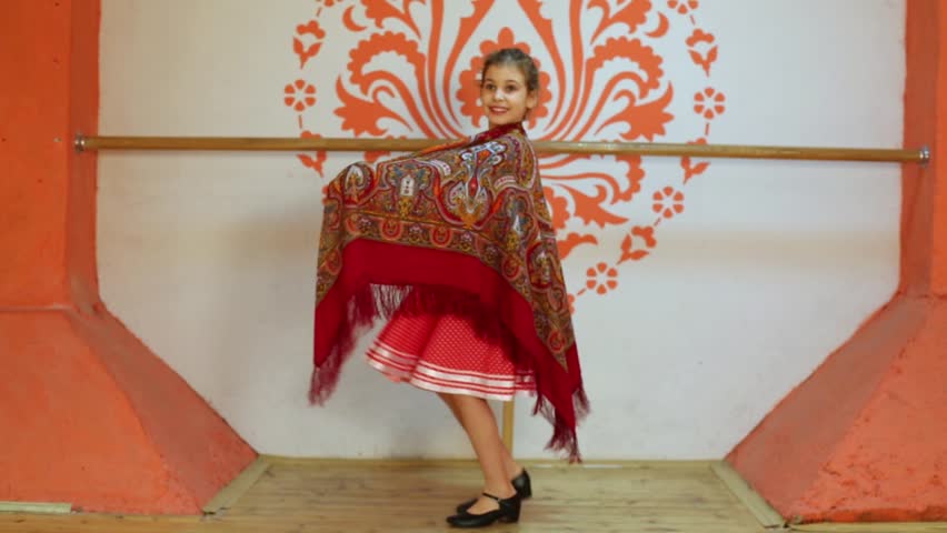 Smiling girl in red folk costume dances with shawl at stage.