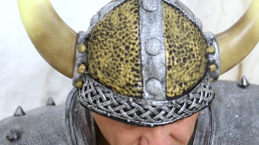 Closeup man in horny viking helmet lifts up his head.