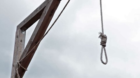 Wooden gallows with swinging noose rope against cloud sky