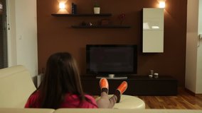 Woman drinking coffee or tea and watching TV at home. TV screen is left empty for greater post production possibilities.