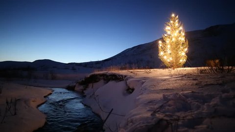 christmas tree glowing lights by mountain stream in winter, snow and blue sky at dawn, Iceland 2