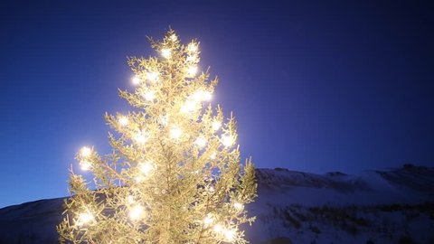 christmas tree glowing lights by mountain in winter dawn, snow and blue sky, Iceland countryside