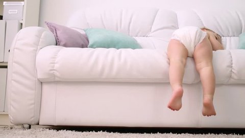 Back of kid in diaper climbing down from white sofa at home