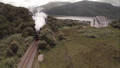 GLENFINNAN, SCOTLAND - JUNE 2014: Stunning aerial shot of the Jacobite Steam Train passing a small church set among stunning scenary in the Scottish highlands