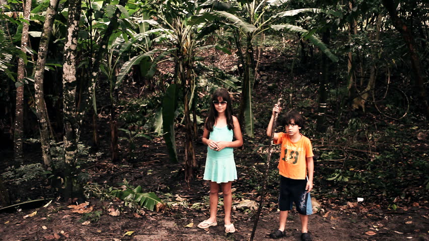 Two funny little kids with sunglasses and stick standing in the jungle