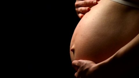 Woman's hand caressing her nude pregnant belly, black background. Female hand on tummy of expectant mother. Gravid girl rubbing her big naked abdomen, close-up. HD video footage 1920x1080p