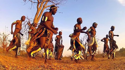 Traditionally dressed African tribesmen of the Herero Tribe dance and sing songs of welcome in Victoria Falls, Zimbabwe, Africa. Drumming, jumping, clapping & singing abound amongst this happy group.
