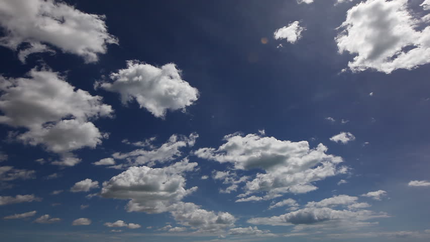 Clouds moving fast in front of a dark blue sky on a sunny summer day