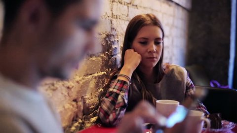 Young bored couple with smartphone sitting in cafe

