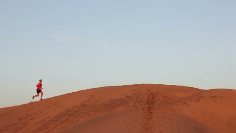 Running man - Jogging athlete runner in desert sand dunes. Fit athletic male fitness model training. Sport in amazing extreme desert landscape nature at sunset