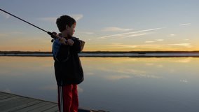 Little boy fishing by himself at sunset on a beautiful colorful scene 4k stock video clip