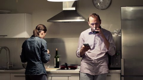 Couple with smartphone cooking and drinking wine in kitchen at home
